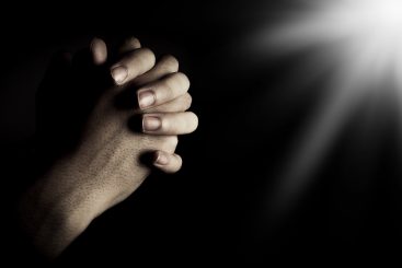 Praying hands is in the dark with light on the hands.
